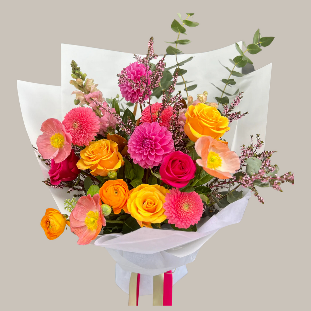 A bright bouquet featuring a variety of seasonal blooms in colors pink, orange, yellow, and green, wrapped in white paper with a pink ribbon. Kenmore Village Florist. Brisbane Flower Delivery.
