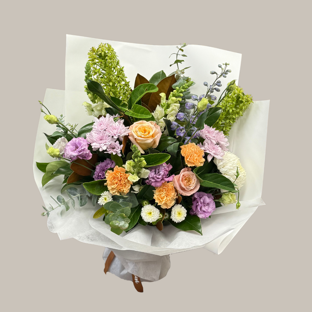 A custom-designed bouquet with a variety of fresh flowers, including roses and other foliage, wrapped in white paper with our signature Kenmore Village Florist ribbon. Brisbane Flower Delivery.