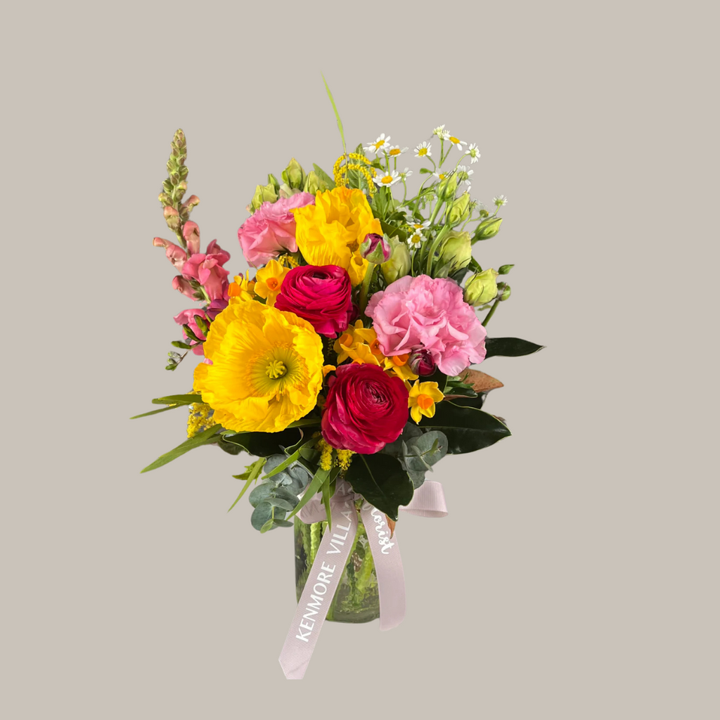 A colorful posy vase arrangement featuring a variety of bright flowers including yellow and pink petals, presented in a clear glass vase adorned with a ribbon. Kenmore Village Florist. Brisbane flower delivery.