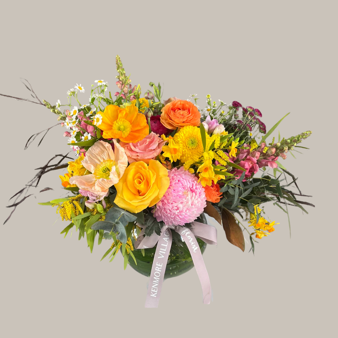 A fishbowl vase arrangement of bright and colorful flowers including yellow, orange, pink, and other colored blooms, with a ribbon decoration. Kenmore Village Florist. Brisbane Same Day Flower Delivery.