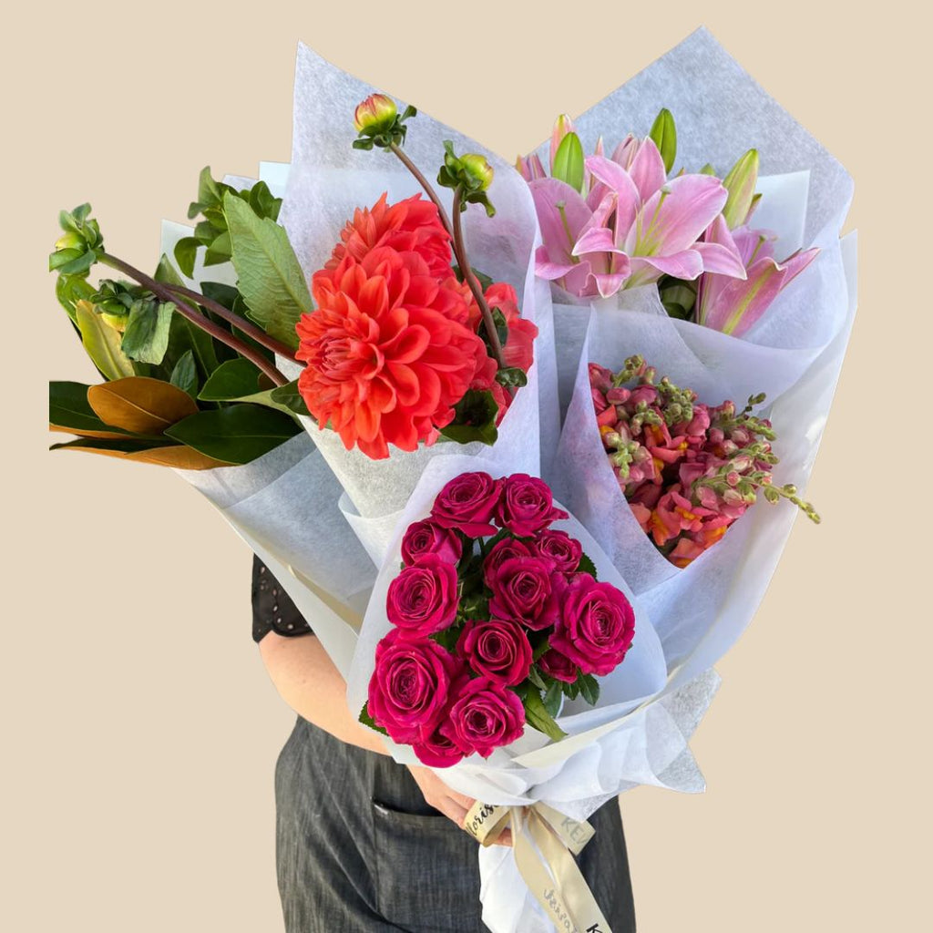 Mixed cut flowers bouquet with red, pink, and purple flowers, wrapped in white paper. Kenmore Village Florist. Brisbane Flower Delivery.