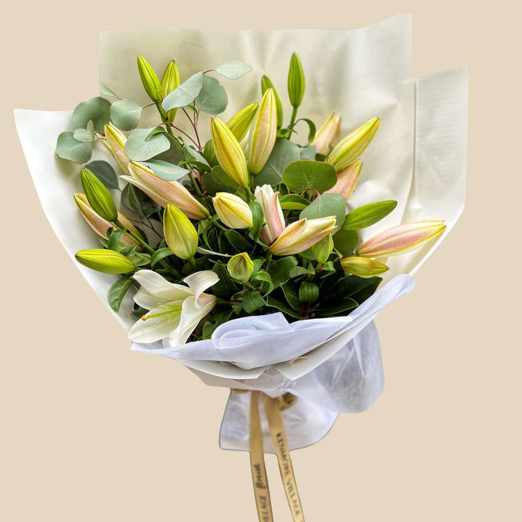 A bouquet of oriental lilies with green leaves, wrapped in white paper with a ribbon.