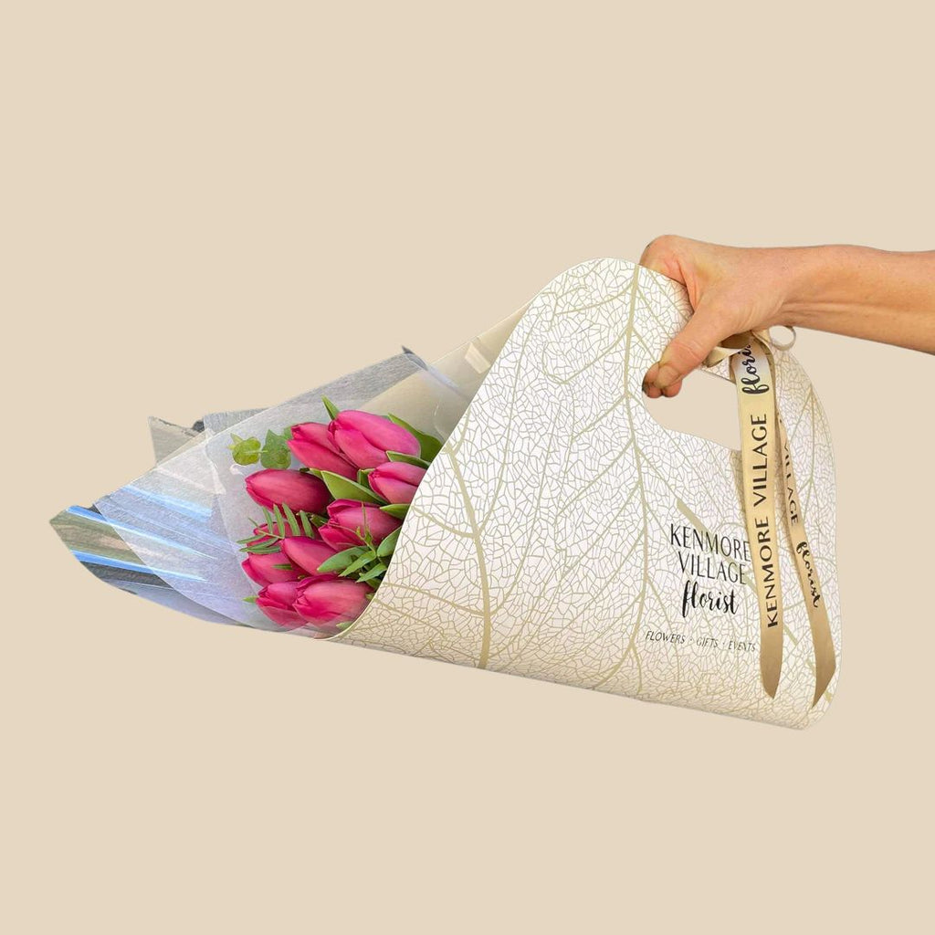 Seasonal wrapped cocoon of pink flowers with the Kenmore Village Florist branding visible on the paper. Brisbane Flower Delivery.