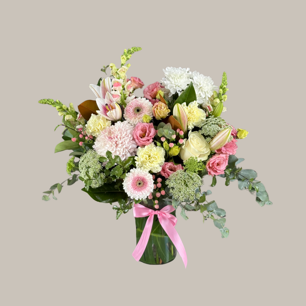 A vase arrangement of fresh flowers featuring pink, white, and green colors, with a pink ribbon decoration. Kenmore Village Florist. Brisbane Flower delivery.