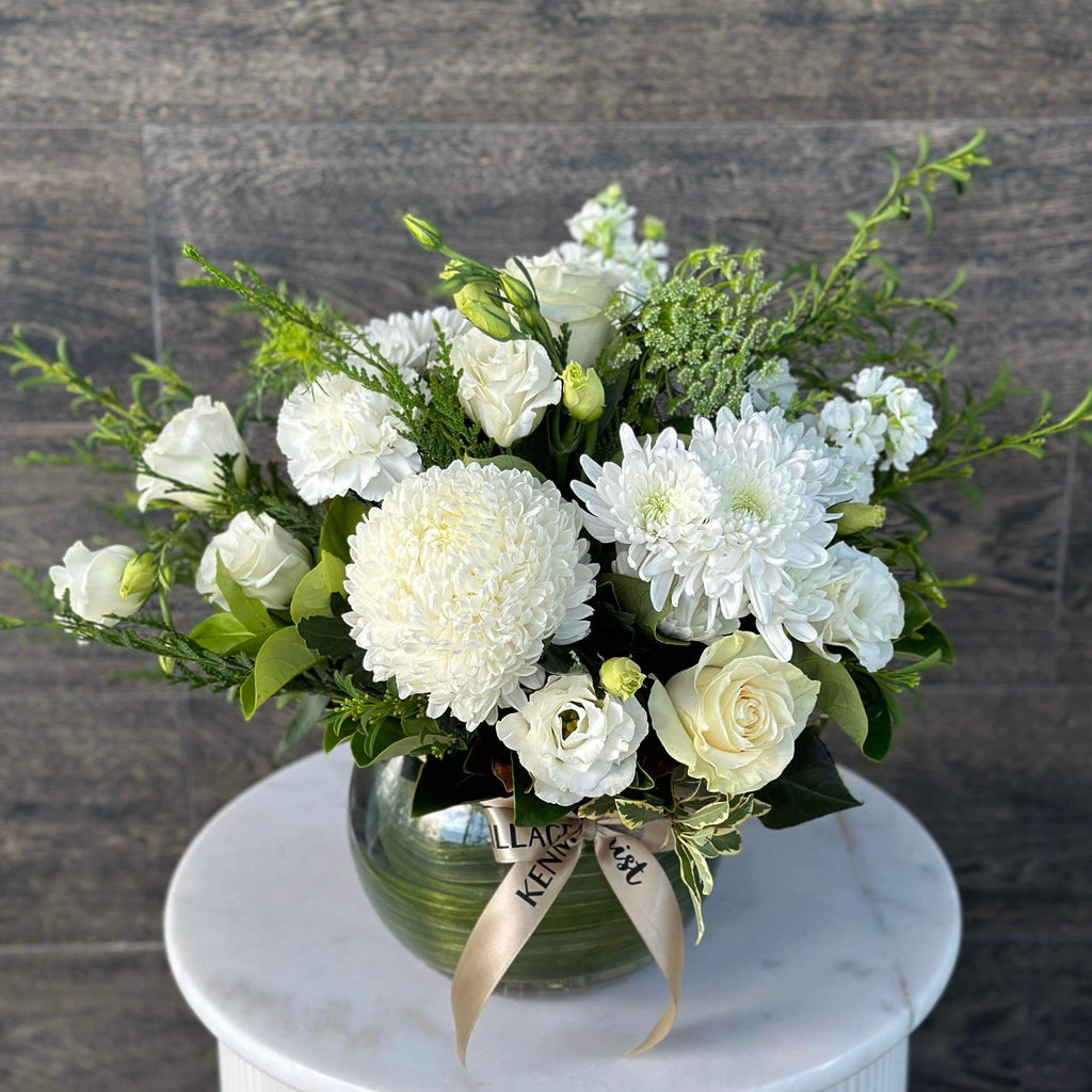 A floral arrangement consisting of white flowers, green foliage, and beige accents. Sympathy Flowers. Kenmore Village Florist. Brisbane Flower Delivery.