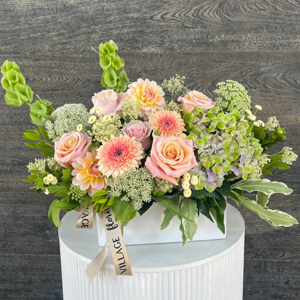 A floral arrangement featuring a mix of pastel seasonal flowers in a white trough. Kenmore Village Florist, Brisbane Flower Delivery.